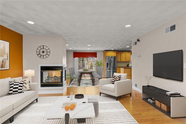 living area with light wood finished floors, baseboards, visible vents, recessed lighting, and a multi sided fireplace
