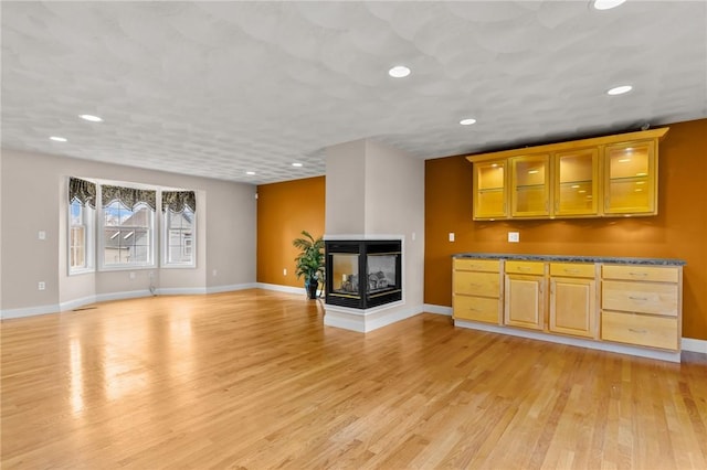 unfurnished living room featuring recessed lighting, baseboards, a multi sided fireplace, and light wood-style flooring