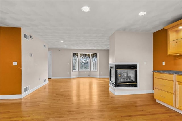 unfurnished living room with baseboards, visible vents, light wood-style floors, and a multi sided fireplace