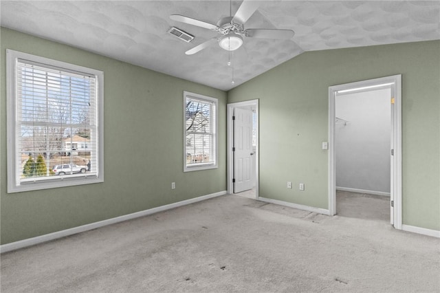 unfurnished bedroom with vaulted ceiling, a walk in closet, carpet, baseboards, and visible vents