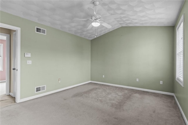 carpeted empty room with vaulted ceiling, visible vents, a ceiling fan, and baseboards