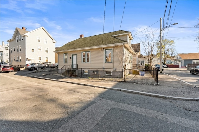 view of front of property featuring a chimney, fence, a residential view, uncovered parking, and roof with shingles