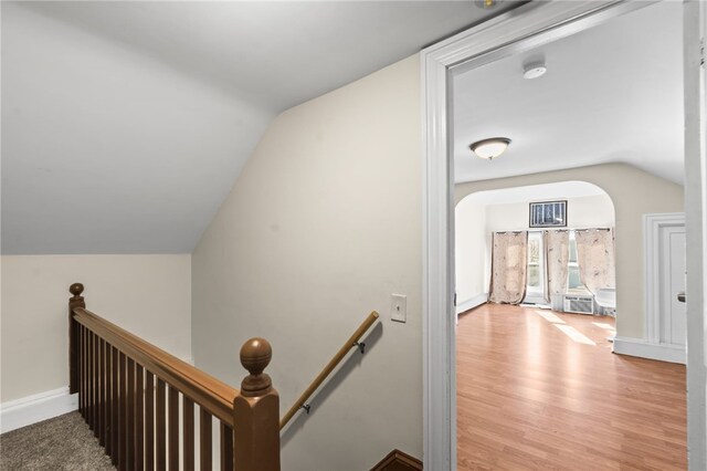 stairway featuring arched walkways, lofted ceiling, wood finished floors, and baseboards