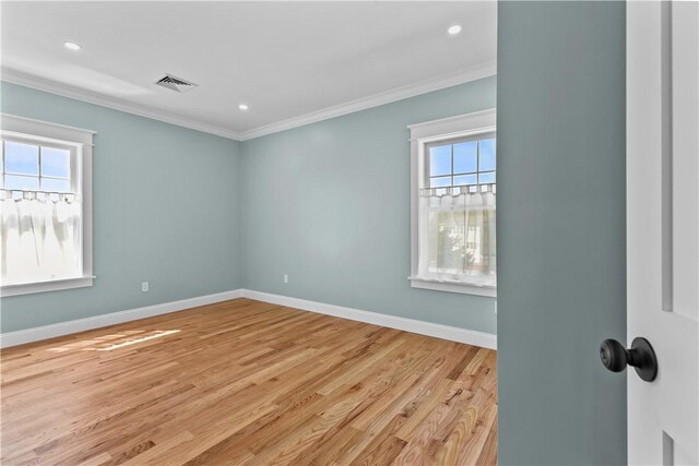 unfurnished room with a wealth of natural light, crown molding, visible vents, and light wood-type flooring