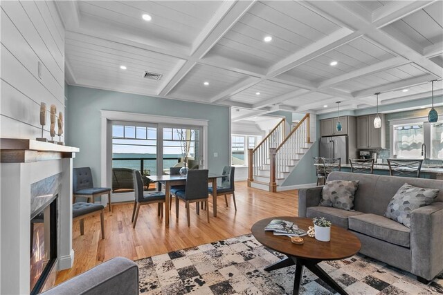 living room with a fireplace, coffered ceiling, stairs, and light wood-style floors