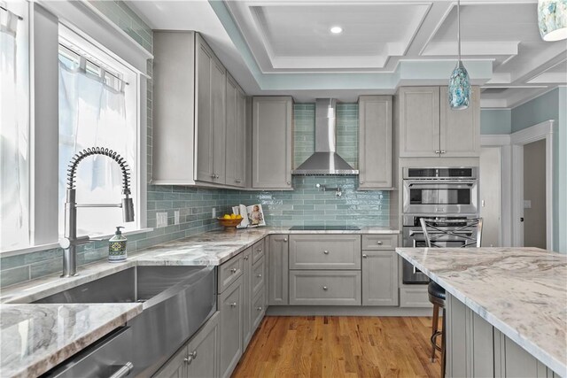 kitchen with wall chimney range hood, appliances with stainless steel finishes, a sink, and gray cabinetry