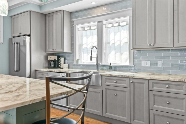 kitchen with light stone counters, high quality fridge, gray cabinets, a sink, and decorative backsplash