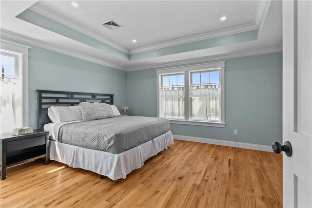bedroom with light wood-style flooring, a tray ceiling, visible vents, baseboards, and crown molding
