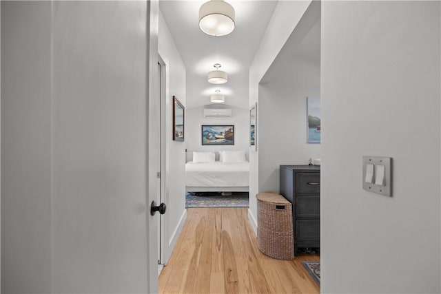 hallway featuring an AC wall unit, baseboards, and light wood finished floors