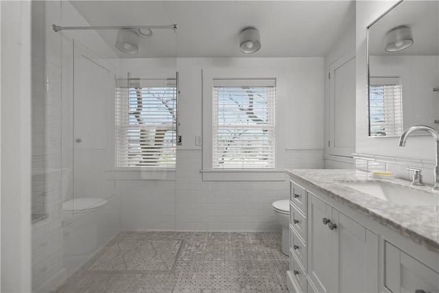 bathroom with speckled floor, toilet, vanity, tile walls, and walk in shower