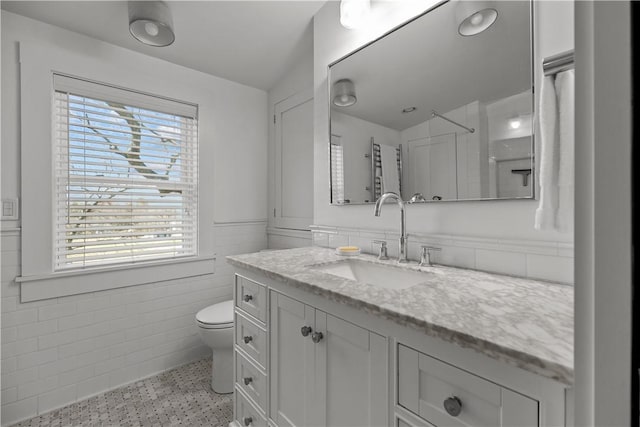 full bathroom with toilet, tile walls, wainscoting, speckled floor, and vanity