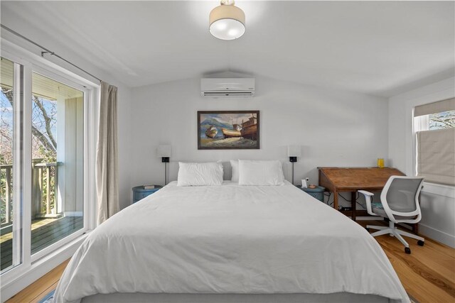 bedroom with wood finished floors, an AC wall unit, vaulted ceiling, and access to exterior