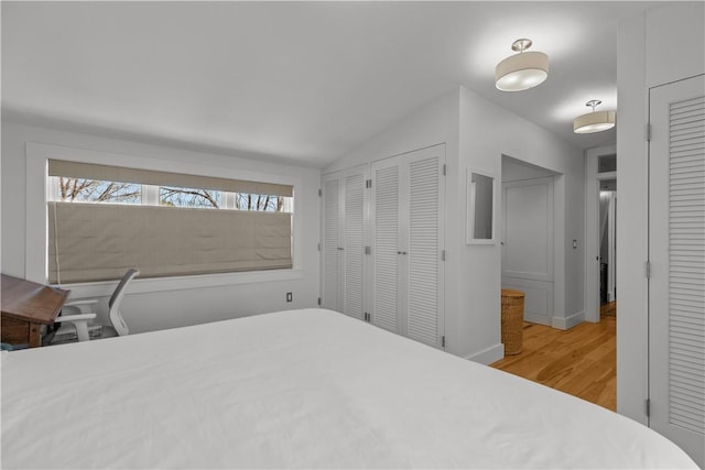bedroom featuring lofted ceiling, wood finished floors, and two closets