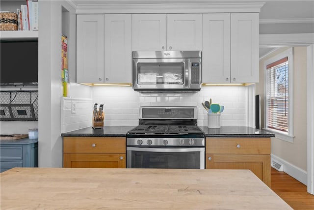 kitchen featuring wood finished floors, ornamental molding, appliances with stainless steel finishes, and tasteful backsplash