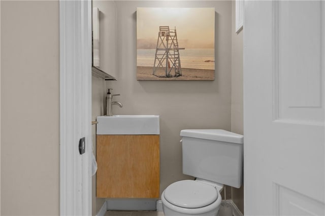half bath featuring baseboards, vanity, and toilet
