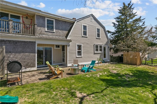 back of property featuring a lawn, a gambrel roof, fence, and a balcony