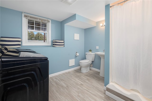 bathroom featuring washer and clothes dryer, wood finished floors, toilet, a shower with curtain, and baseboards