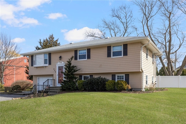 raised ranch with a front lawn, fence, aphalt driveway, and a garage