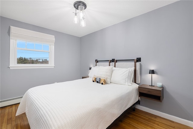 bedroom featuring baseboard heating, baseboards, and wood finished floors