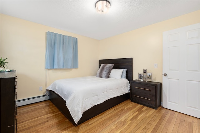 bedroom with a baseboard heating unit and light wood-style floors