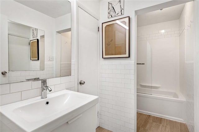 bathroom featuring washtub / shower combination, wood finished floors, a sink, tile walls, and tasteful backsplash