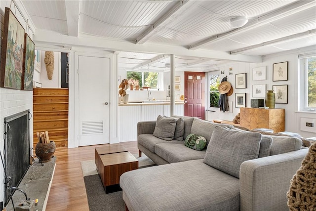 living room featuring a fireplace, a healthy amount of sunlight, beam ceiling, and light wood-type flooring