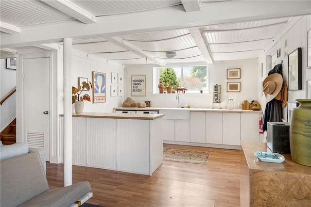 kitchen with light wood finished floors, a peninsula, beam ceiling, a sink, and light countertops