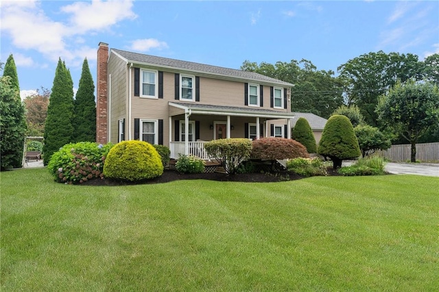 colonial house featuring fence, a front lawn, covered porch, and a chimney