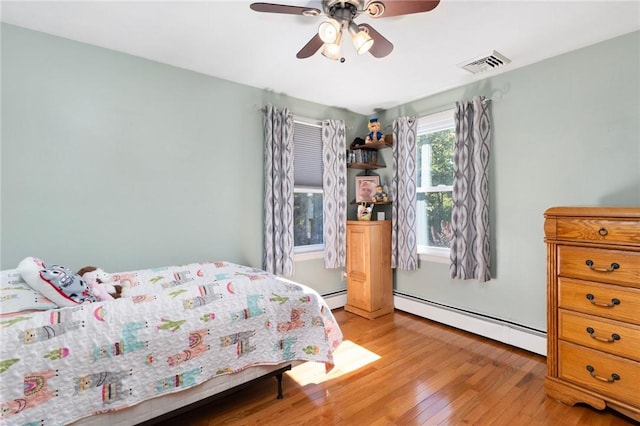 bedroom with baseboard heating, a ceiling fan, light wood-style floors, and visible vents