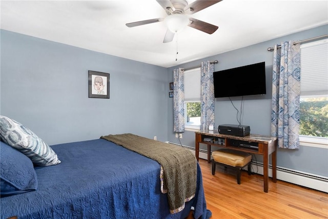 bedroom with a baseboard radiator, wood finished floors, ceiling fan, and multiple windows