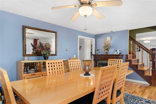 dining area featuring visible vents, a ceiling fan, wood finished floors, stairs, and a fireplace