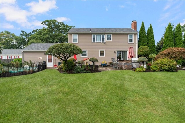 rear view of property with fence, a lawn, a chimney, and a patio area