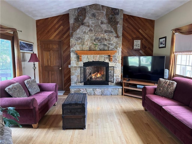 living area with wooden walls, a stone fireplace, an accent wall, and wood finished floors