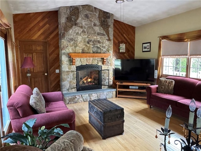 living room featuring lofted ceiling, a stone fireplace, wood walls, and wood finished floors