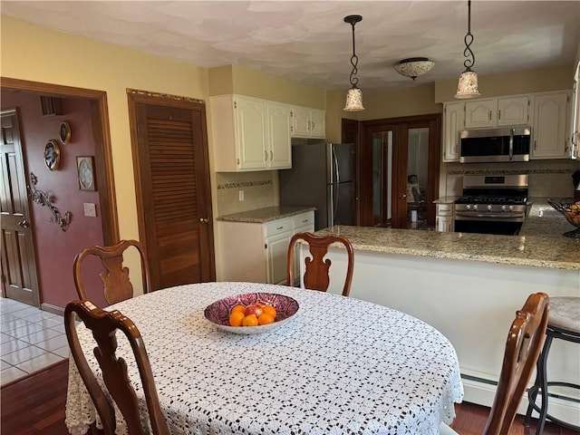 kitchen featuring white cabinets, a peninsula, light stone counters, appliances with stainless steel finishes, and hanging light fixtures