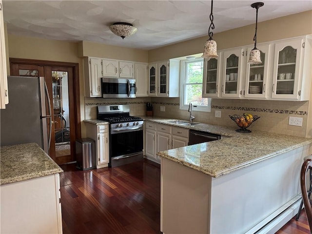 kitchen featuring stainless steel appliances, a peninsula, a sink, decorative backsplash, and glass insert cabinets