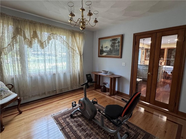 exercise area featuring french doors, a chandelier, and light wood-type flooring
