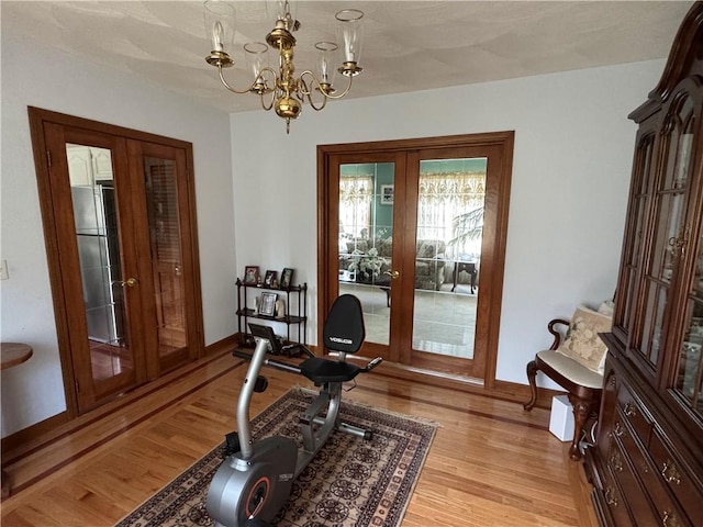 exercise area featuring an inviting chandelier, light wood finished floors, baseboards, and french doors