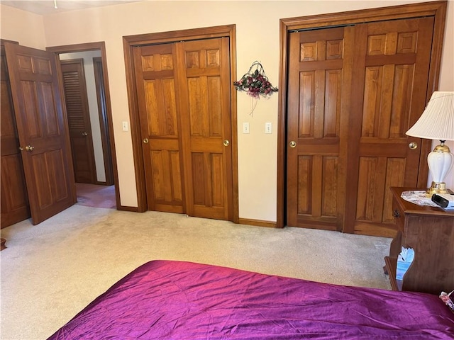 bedroom featuring two closets, baseboards, and carpet flooring