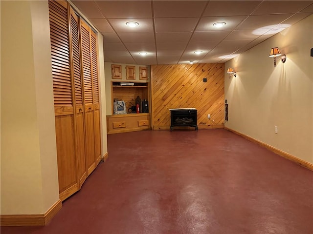 finished basement with baseboards, wood walls, a wood stove, and recessed lighting