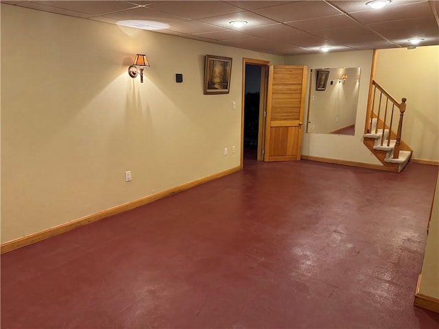 finished basement featuring a paneled ceiling, baseboards, and stairs