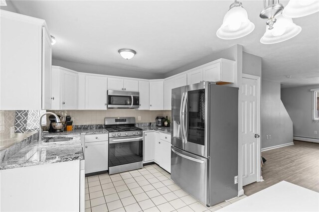 kitchen featuring white cabinets, stainless steel appliances, a sink, light stone countertops, and decorative backsplash
