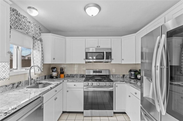 kitchen with appliances with stainless steel finishes, light stone countertops, a sink, and white cabinetry