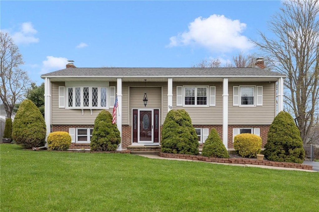 split foyer home featuring a front lawn, a chimney, and brick siding