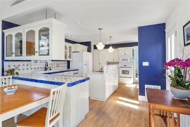 kitchen featuring light wood finished floors, decorative backsplash, white appliances, and white cabinetry