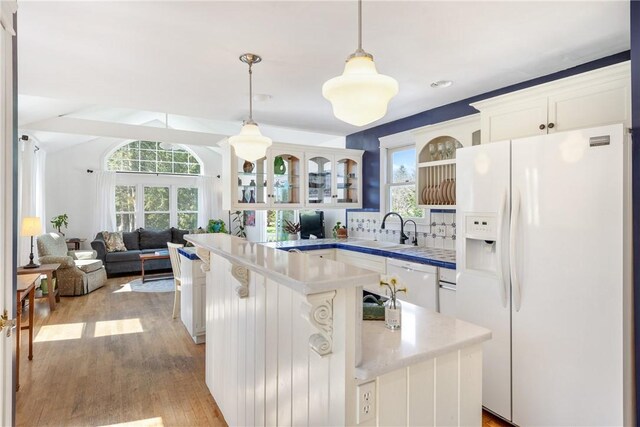 kitchen with a sink, glass insert cabinets, white appliances, light countertops, and decorative light fixtures