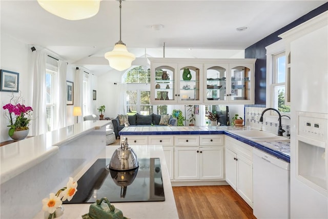 kitchen featuring dishwasher, a sink, pendant lighting, a peninsula, and glass insert cabinets