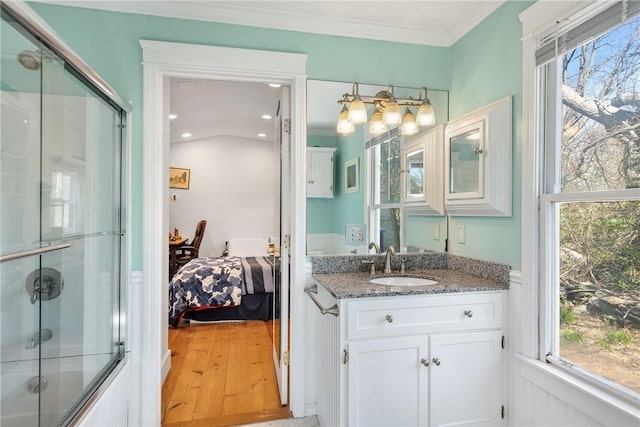 bathroom featuring wood finished floors, vanity, ornamental molding, ensuite bath, and bath / shower combo with glass door