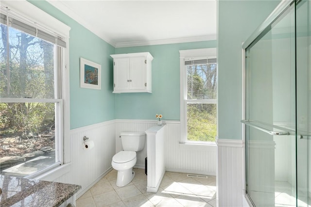 bathroom with tile patterned floors, visible vents, toilet, crown molding, and wainscoting