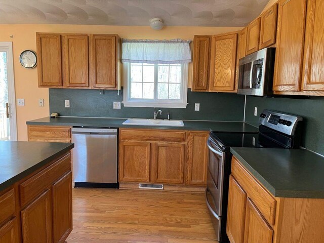 kitchen with dark countertops, a sink, light wood-style floors, and appliances with stainless steel finishes
